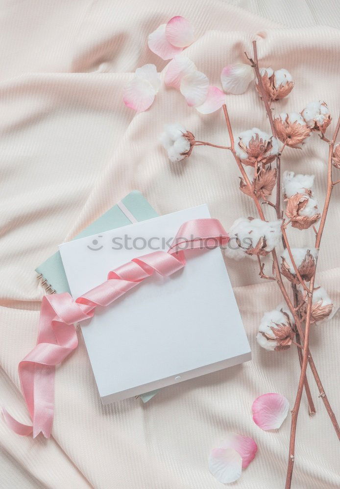 Aesthetic lifestyle. Notebook, white box with pink ribbon. Beige fabric background with cotton branches.  Top view.