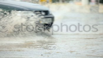 Similar – Whoosh!!! There thunders the dark car full through a deep puddle. A huge shower of water drenches the pedestrian with a colorful umbrella and red rubber boots.