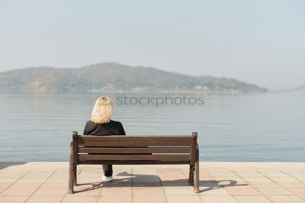 Rear view of a woman sitting on a wooden bench and looking at a lake