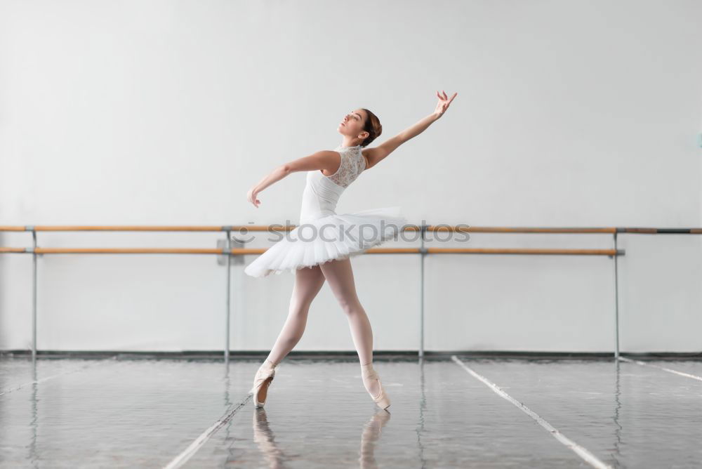 Elegante Ballerina in weißem Kleid tanzt gegen eine rustikale Wand