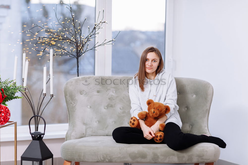 Foto Bild Junge Frau sitzt mit einem Tablet auf einem kleinen Hund auf einem grauen Sofa