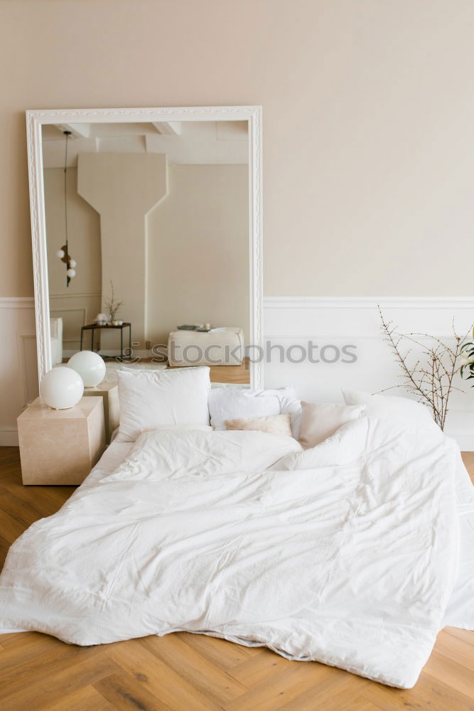 Ein Doppelbett mit weißer Bettwäsche und beigen Kissen in einem hellen skandinavischen Schlafzimmer, ein Bett auf dem Boden und Blumen in einer Vase