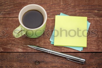 Green slip of paper with pen, a cup of coffee and a potted plant