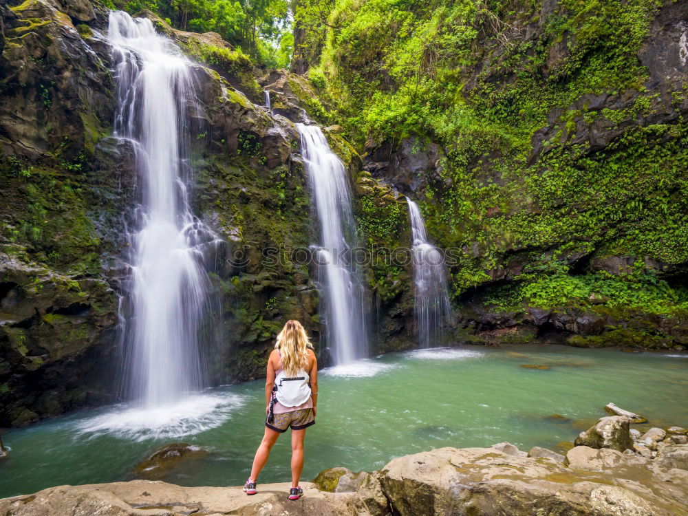 young woman standing in front of tropical waterfall