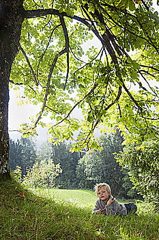 Attraktive blonde Frau sitzt auf weißer Bank unter einer Eiche an einem Teich