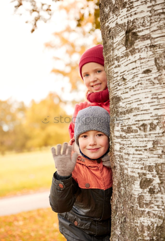 Two adorable young brothers outdoors in winter wrapped up warmly against the chill weather with the older boy cuddling his toddler sibling on his lap