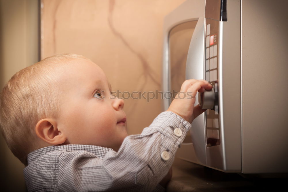 Baby toddler sits interested and curious in front of washing machine on the floor