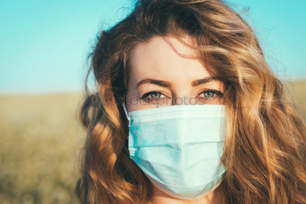 Young woman in medical mask standing near blooming flowers