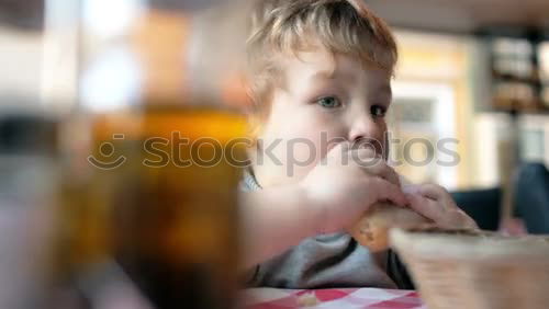 Similar – Little boy in a cafe during lunch. Hungry kid eating sausage from his sandwich