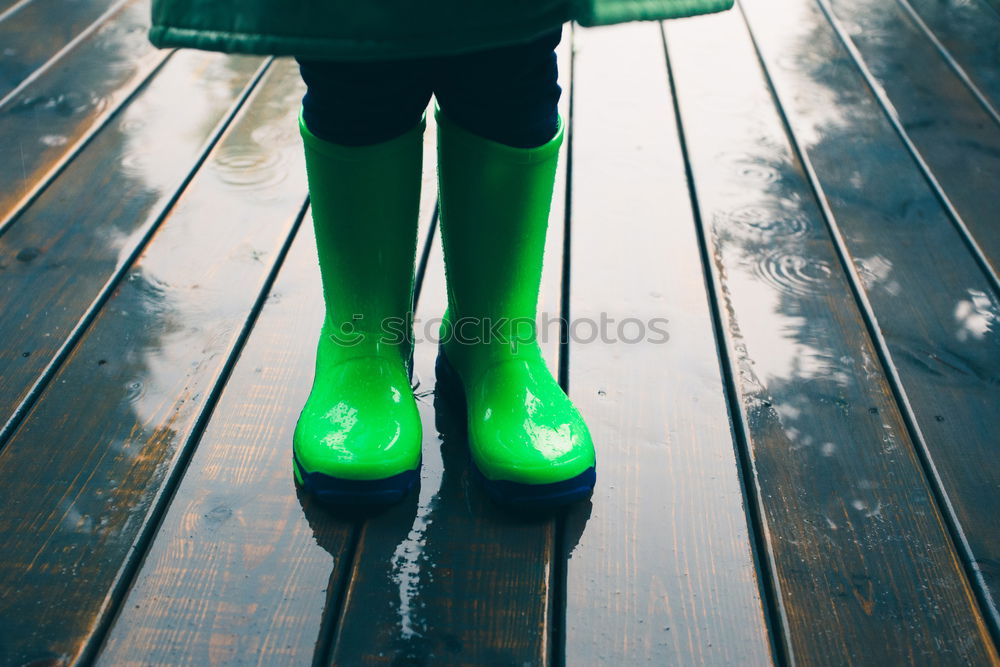 Kid standing on a porch wearing green wellies and raincoat