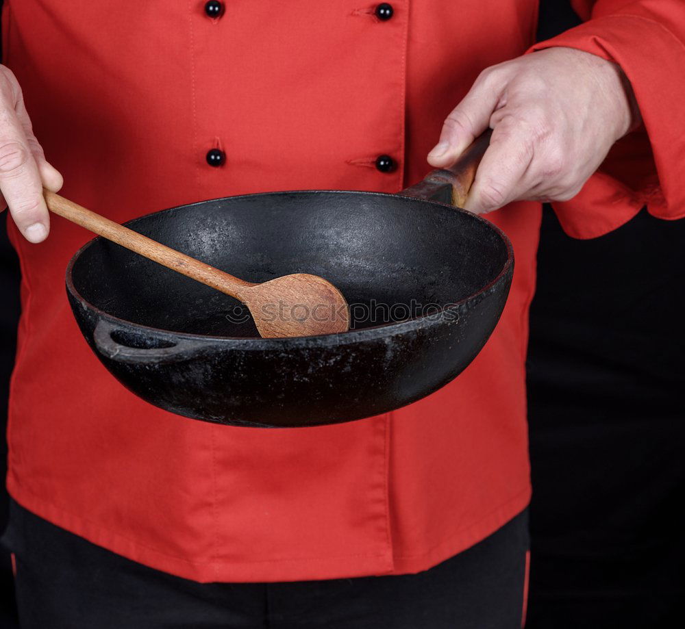 cook in red uniform holding an empty black frying pan