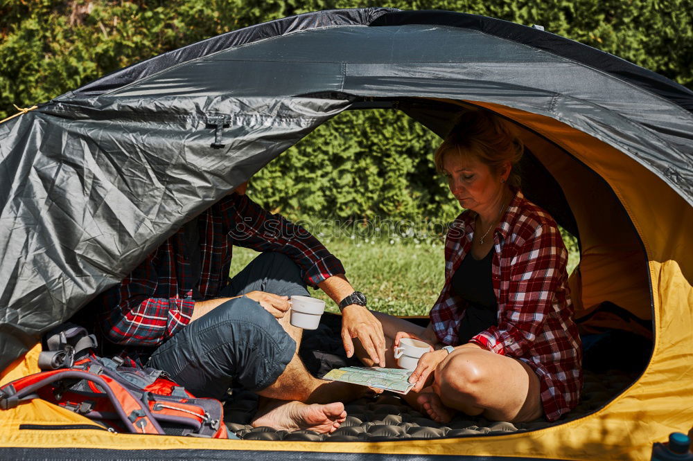 Couple planning next trip while sitting with map in tent. People relaxing in tent at camping during summer vacation