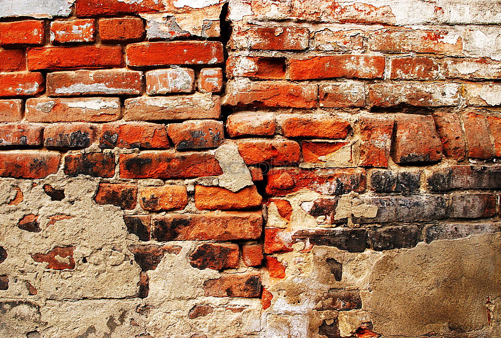 Abgefallener Putz an Backsteinwand. Verwitterte  Wand aus Backstein, Naturstein und marodem Putz. Sanierungsbedürftig