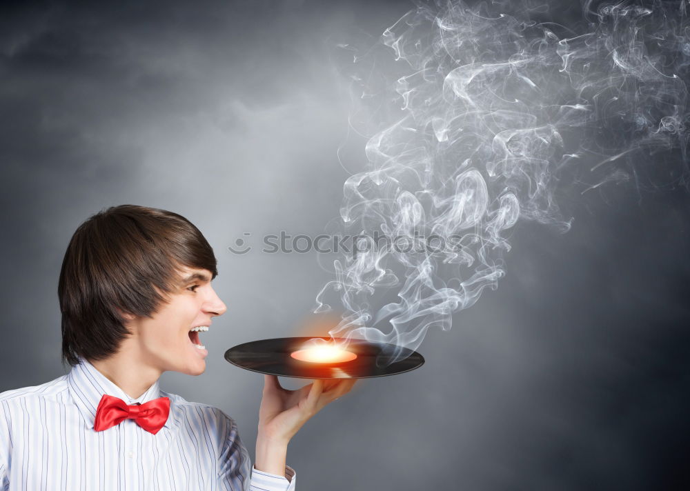 Young man vaping, studio shot. Bearded guy with sunglasses blowing a cloud of smoke on black background. Concept of smoking and steam without nicotine.