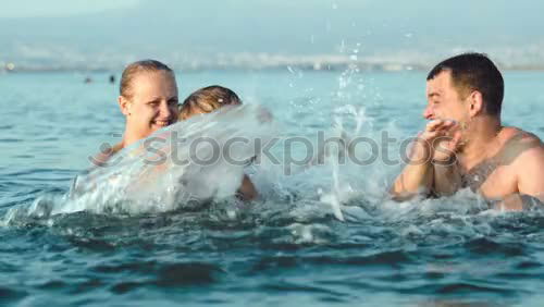 Similar – Laughing little boy flanked by his loving parents paddling together in the shallow water at the edge of the sea