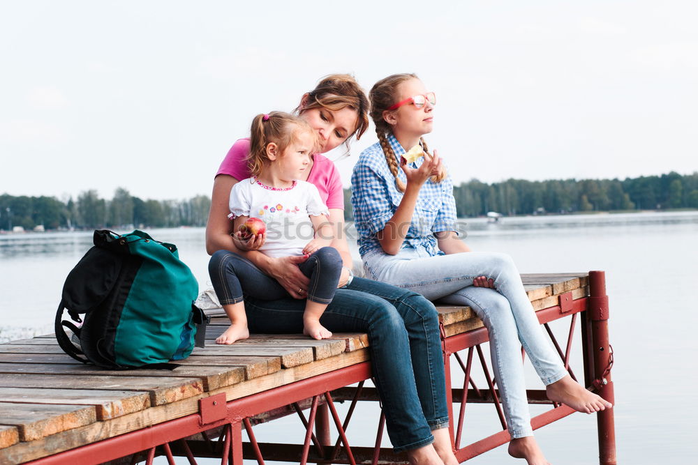 Family spending vacation time together having a snack sitting on jetty over the lake on sunny day in the summertime