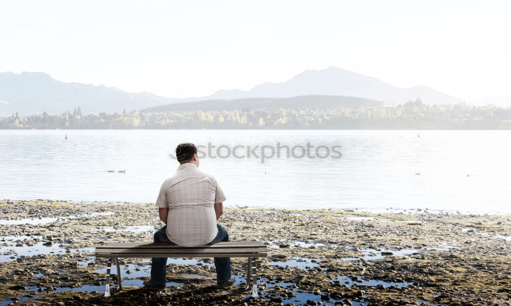 Similar – Rear view of a woman sitting on a wooden bench and looking at a lake