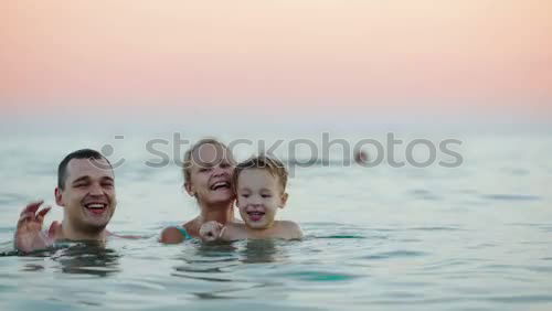 Laughing little boy flanked by his loving parents paddling together in the shallow water at the edge of the sea