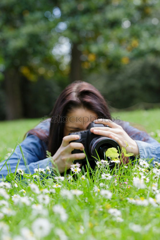 Smiling young woman using a camera to take photo at the park.