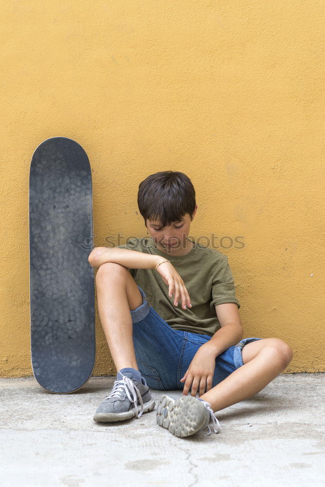 Similar – Image, Stock Photo Front view of young boy sitting on ground leaning on a yellow wall while using a mobile phone to listening music