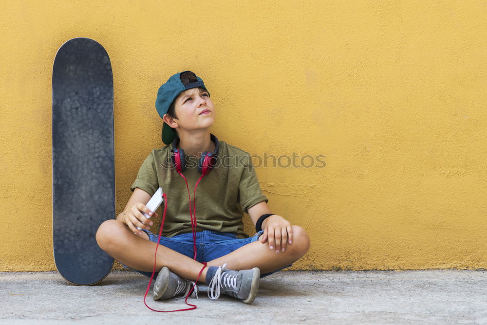 boy sitting on ground leaning on a wall, taking a selfie