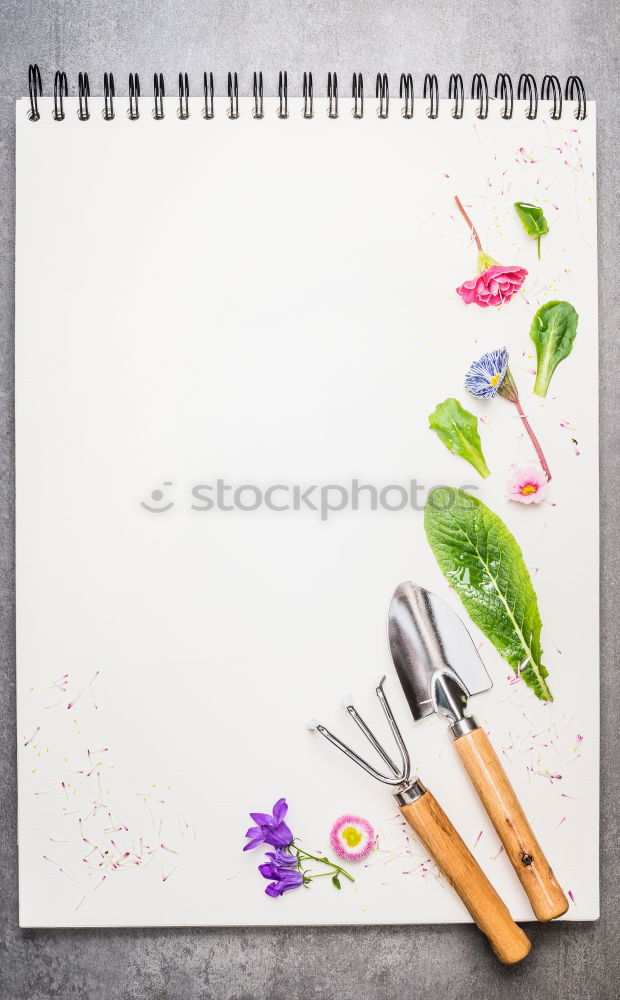 Garden tools with flower parts on empty notebook .