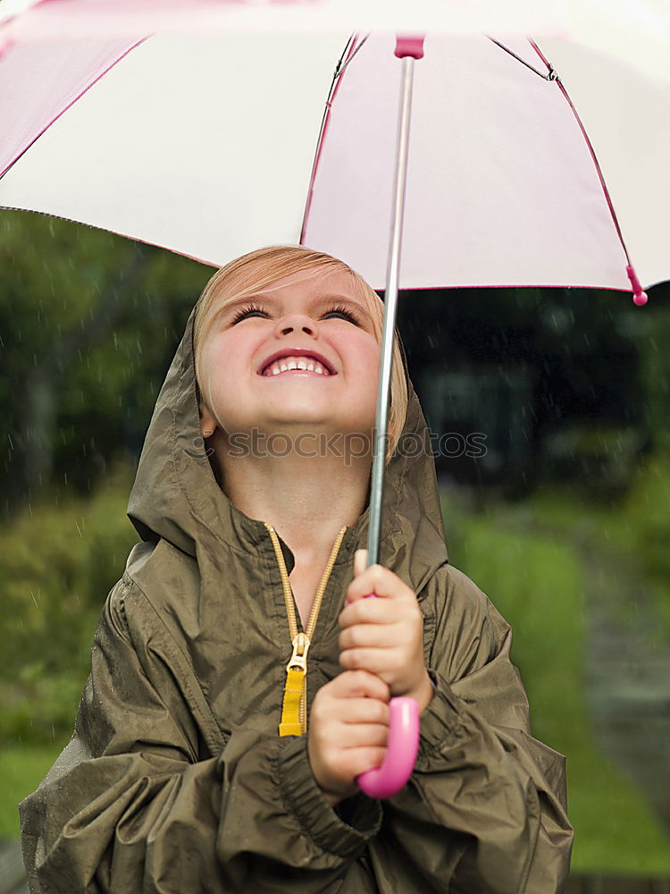 Image, Stock Photo Child in a raincoat with umbrella crouched down playing and laughing in a puddle