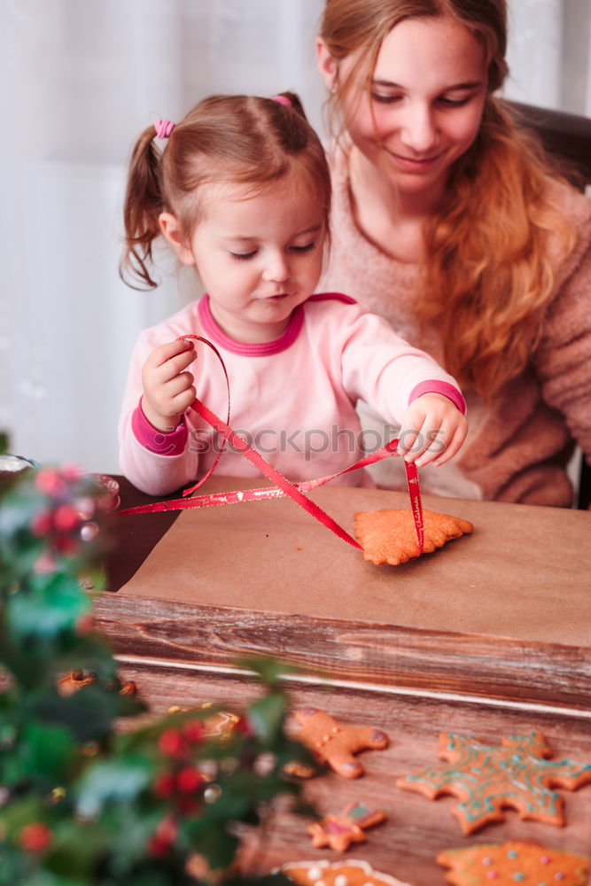 Girls tying baked Christmas gingerbread cookies with ribbon