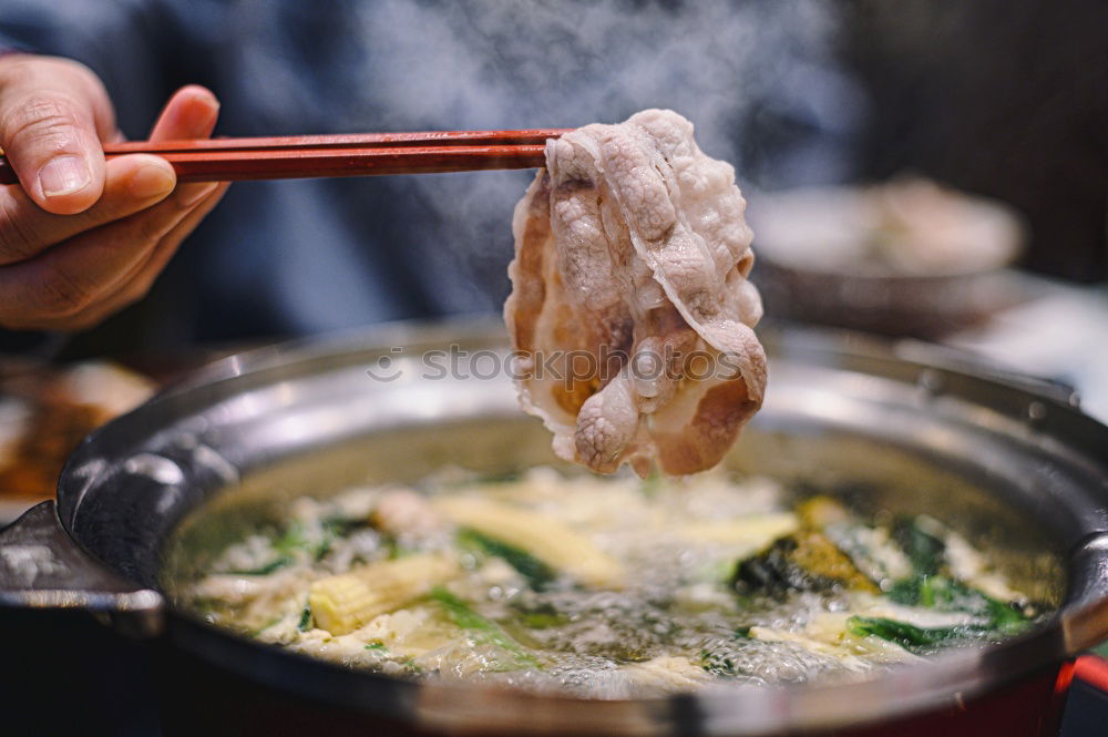 Korean hot pot and people taking food with chopsticks.