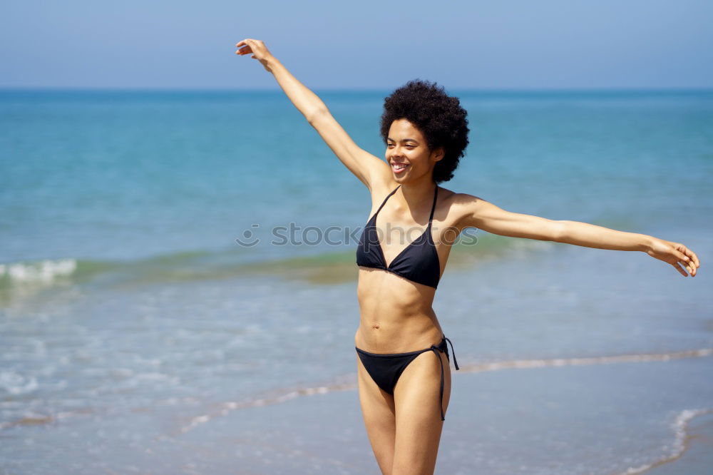 Young woman in bikini on a tropical beach with open arms.