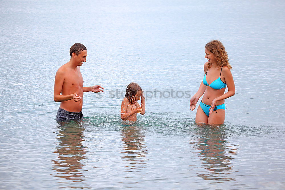 Similar – Laughing little boy flanked by his loving parents paddling together in the shallow water at the edge of the sea