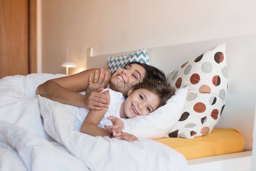 Three sisters playing with each other lying down in bed at home listening to music