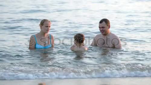 Similar – Image, Stock Photo Young family enjoying the sea at sunset paddling in the shallows together playing with the ball as they enjoy their summer vacation