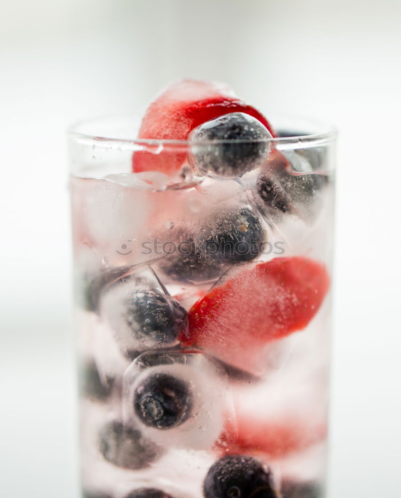 Berry-fruity water, iced with raspberries, blueberries, ice cubes and drinking straw on white background