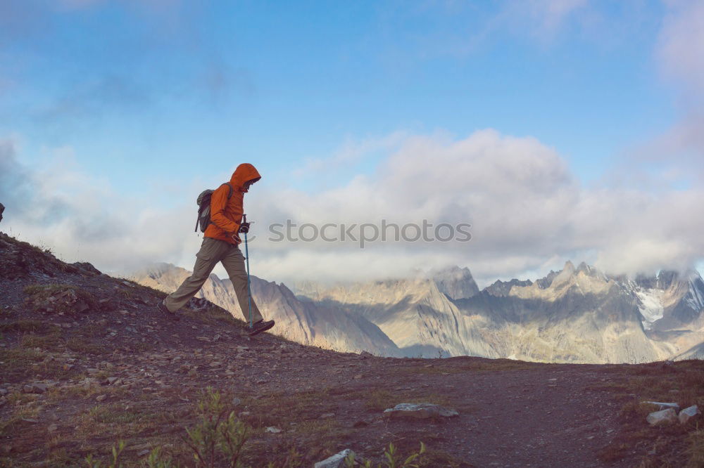 Similar – Cloud rolls over the mountains, man with red jacket and backpack stands on a path and looks into a valley