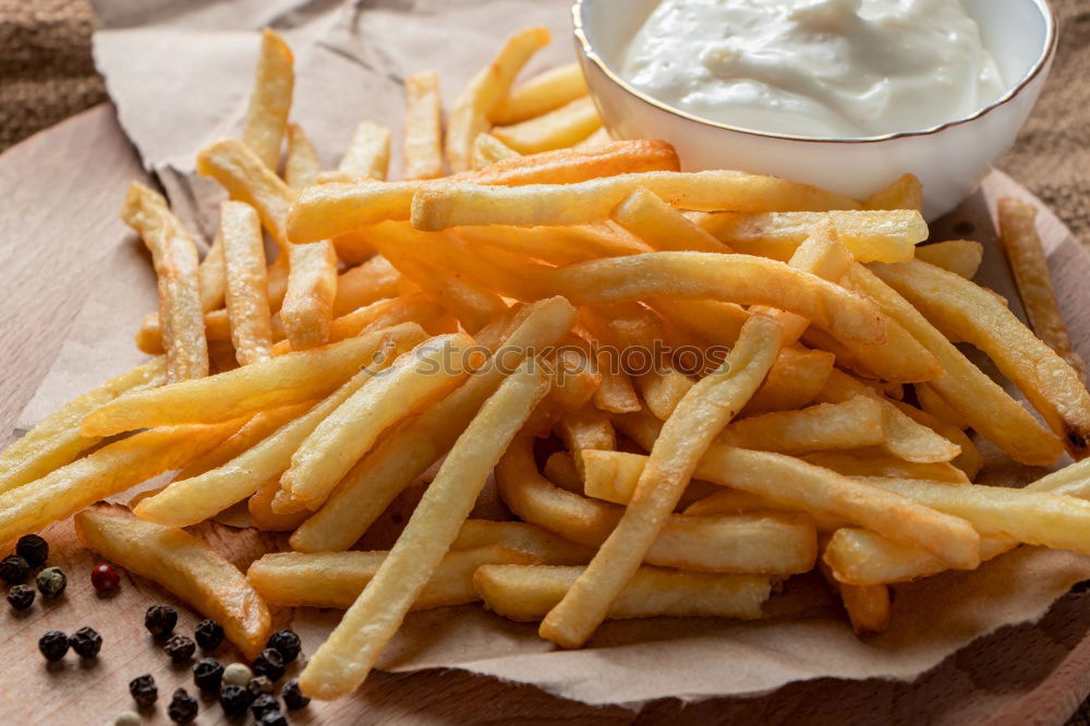 Foto Bild Portion Pommes mit Mayonnaise in einem Pappschälchen und einer Holzgabel auf einem Holztisch