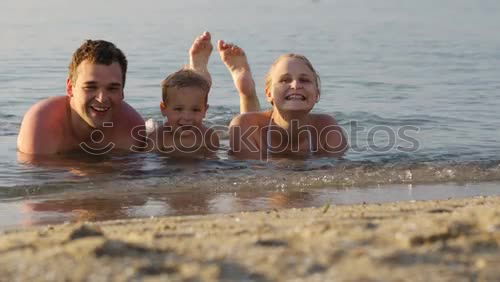 Similar – Laughing little boy flanked by his loving parents paddling together in the shallow water at the edge of the sea