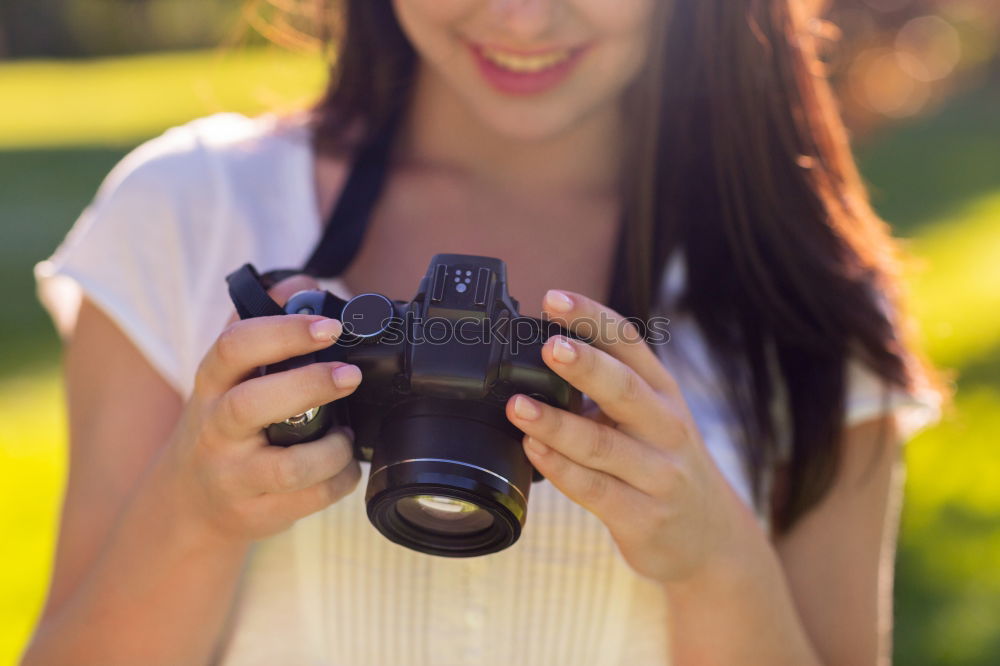 Smiling young woman using a camera to take photo at the park.