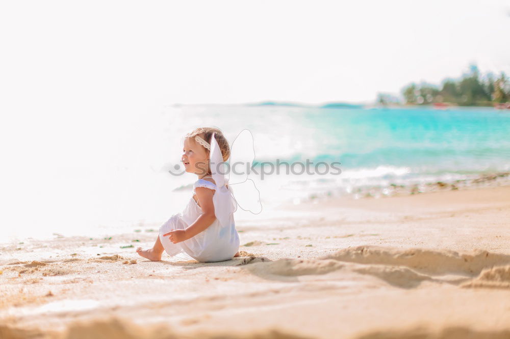 Süßes fröhliches kleines Mädchen, das im Badeanzug am Strand mit Sand spielt, ein Herz zeichnet und schreibt. Wunderschöner Sommersonnenuntergang, Meer, Kokospalmen, malerische exotische Landschaft. Phuket, Thailand