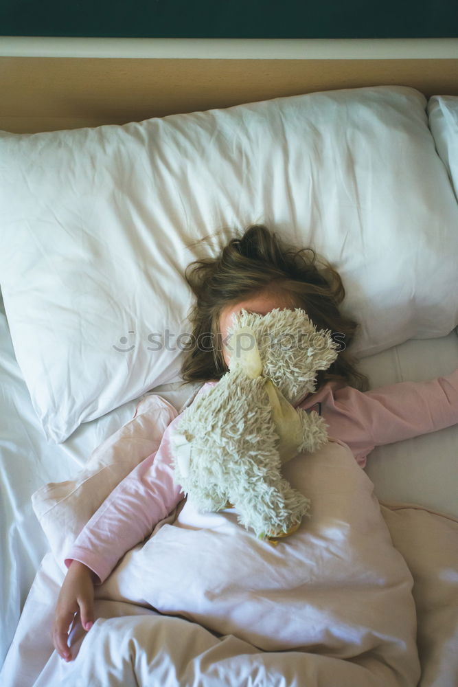 Little girl lying in a bed with teddy bear at the morning