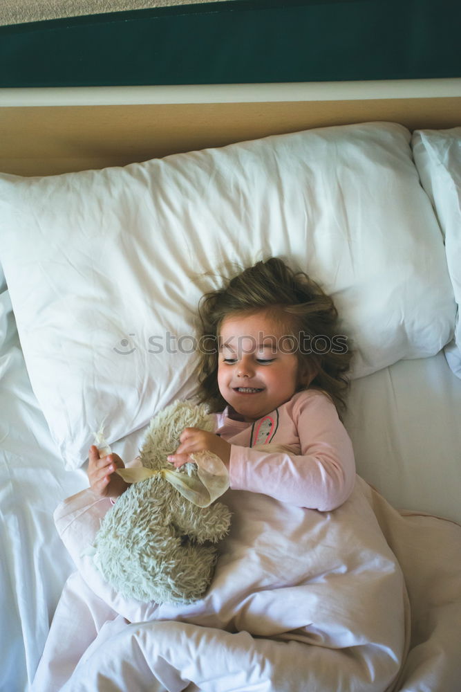 Little girl lying in a bed with teddy bear at the morning