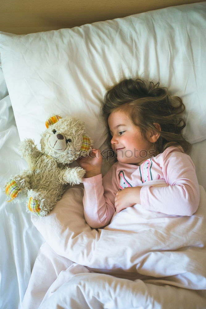 Little girl lying in a bed with teddy bear at the morning