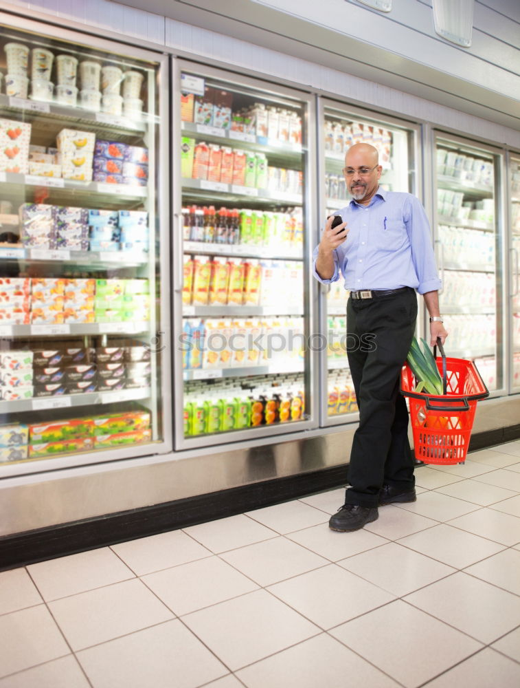 Image, Stock Photo A smiling middle aged woman in a light blue shirt is standing in a household section of a supermarket. She is holding a tablet and a red shopping basket in her hands. A woman is looking at the shelves, searching for something particular