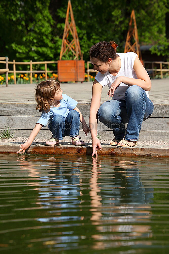 Young boy and his little sister sitting on jetty over the lake and dipping feet in water on sunny day in the summertime