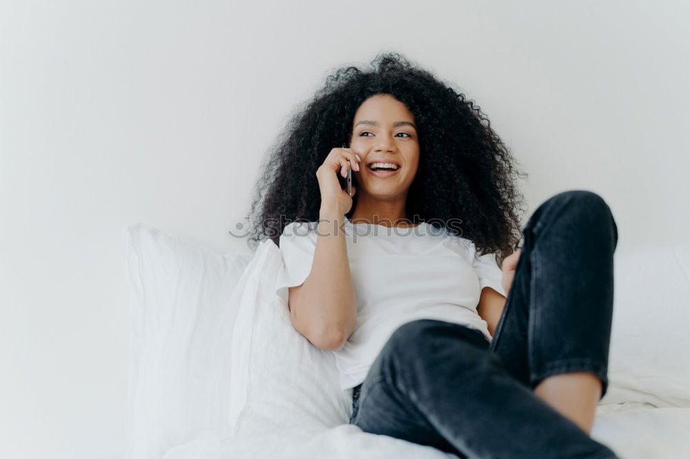 close up of a pretty black woman with curly hair smiling and lying on bed looking away