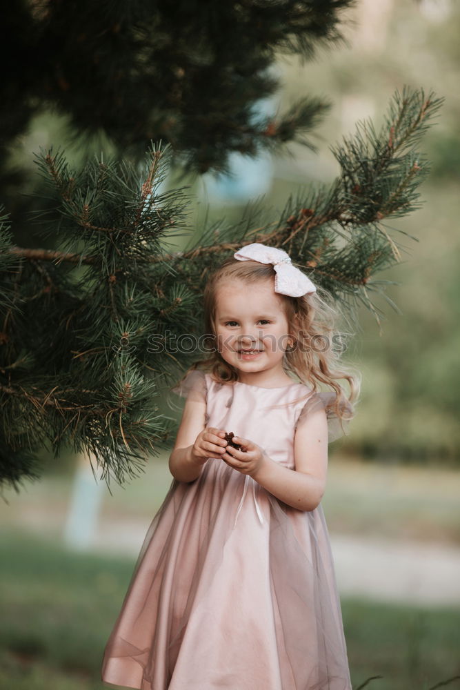 little cute girl have fun under tree with cones on a sunny spring day