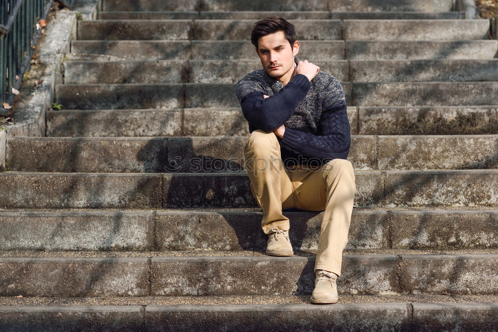 Young man with modern hairstyle sitting on stairs