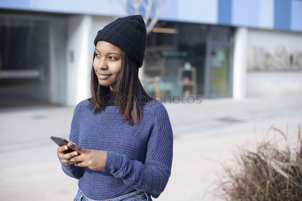 Happy woman with hat in city street, while using technology