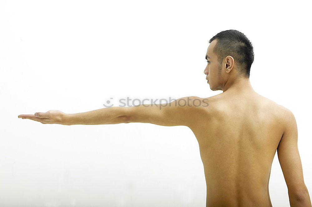 young woman with very short hair stands naked in front of light turquoise wall in pose with half raised arms