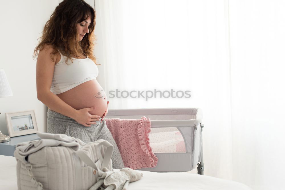 Happy pregnant woman sitting and touching her belly at home